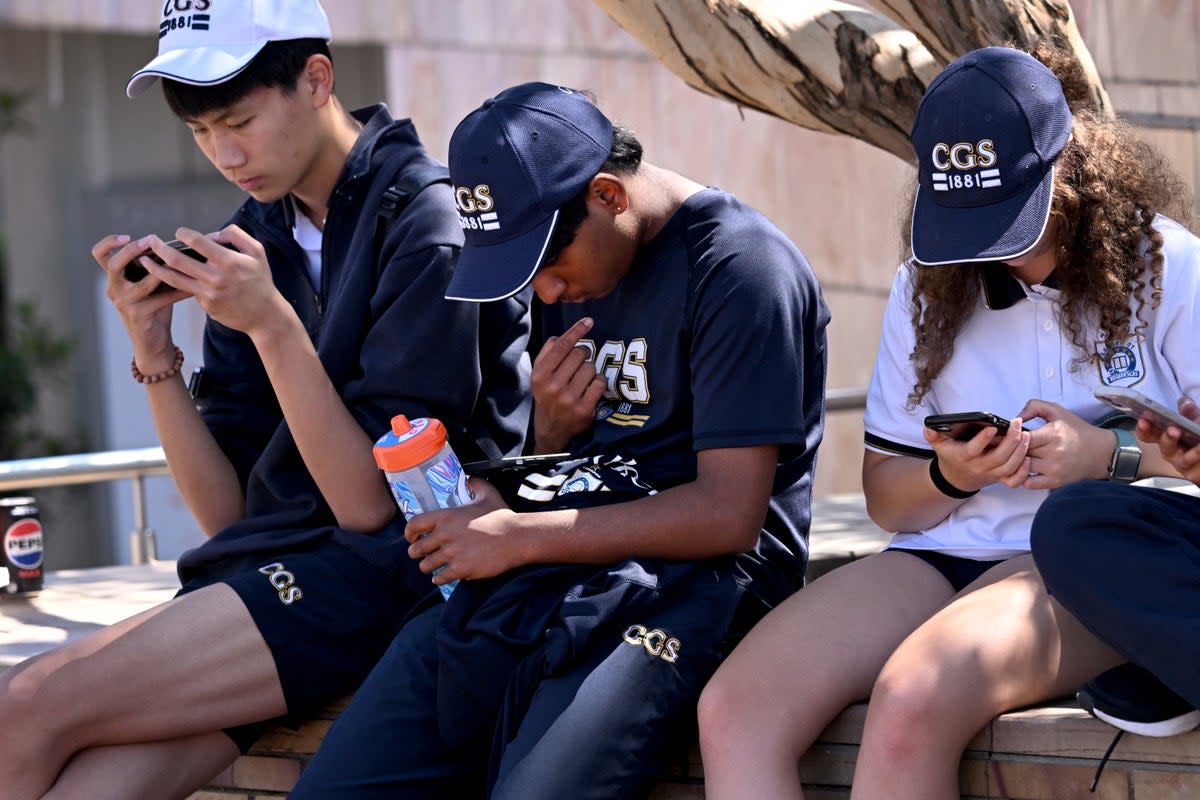 Pelajar melihat telefon mereka di Melbourne, 28 November 2024 (AFP melalui Getty Images)